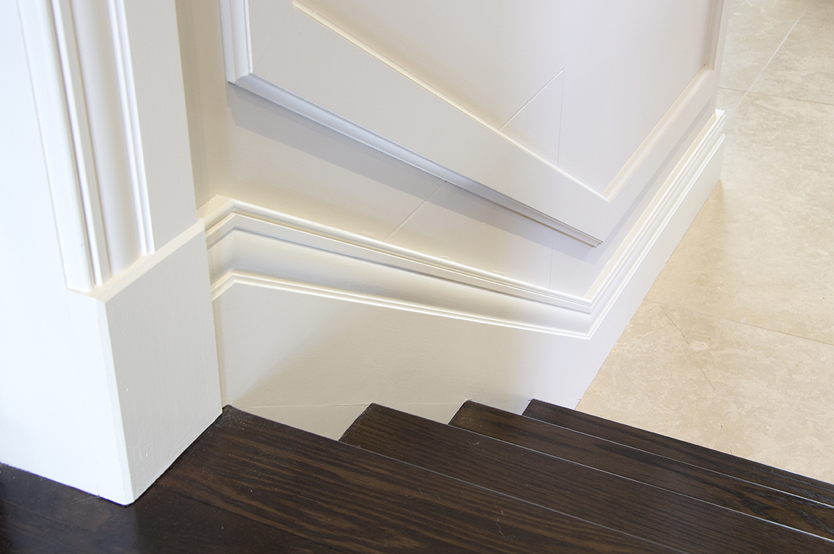 White timber skirting block resolving the junction between a fluted door architrave and a deep stepped skirting board at the base of a staircase.