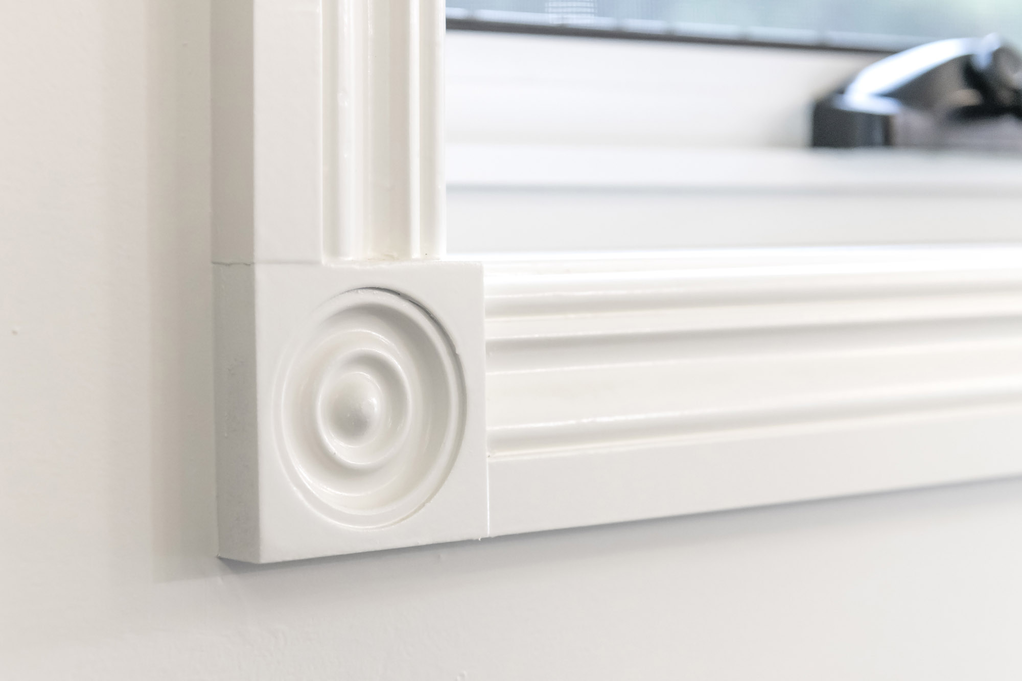 White painted rosette corner block resolving the bottom corner of a fluted timber window architrave, a traditional heritage detail.