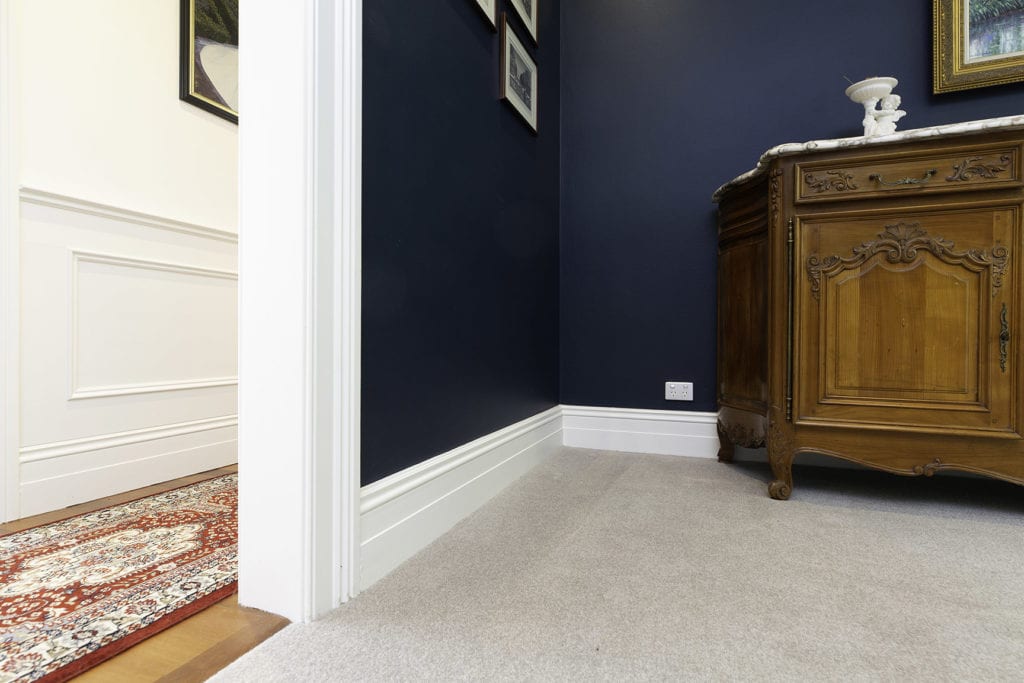 Close-up of white timber skirting boards in a hallway with navy walls