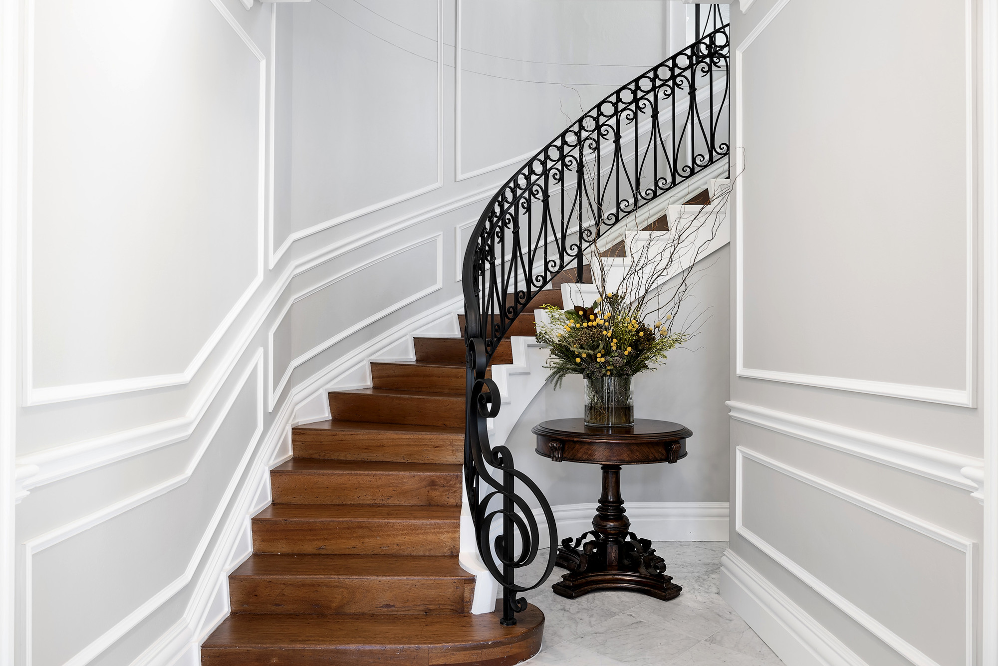 Curved staircase with timber treads, ornate black wrought iron balustrade, and classic wall panelling throughout
