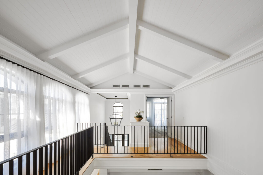 Spacious landing area with black, vertical railing and Country Farmhouse-style accented ceiling beams