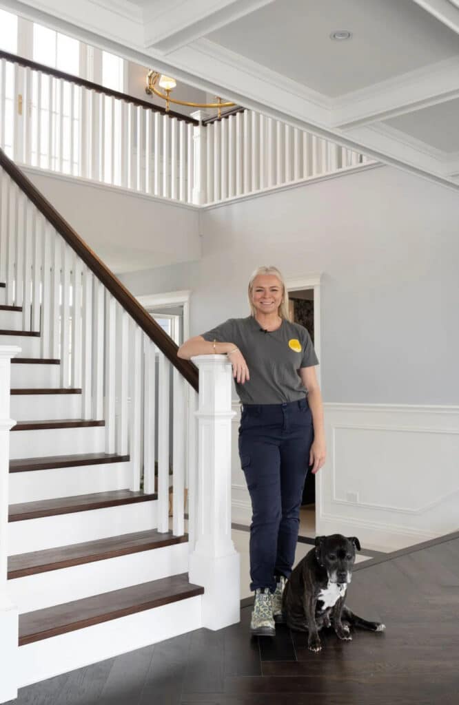 Rachael Turner of Front Porch Properties leaning against a banister in a modern entryway with a black and white dog by her feet.