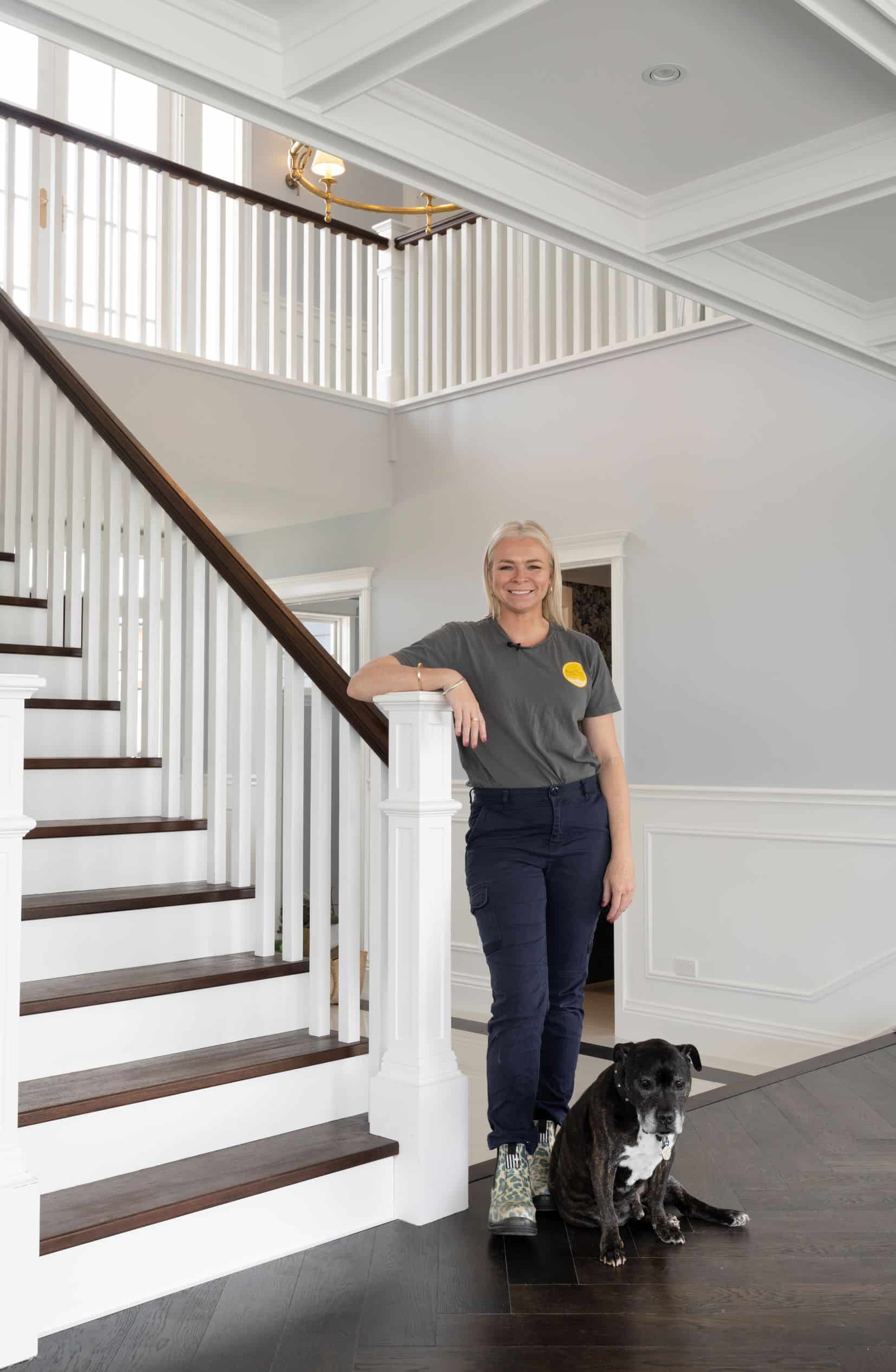 Rachael Turner of Front Porch Properties leaning against a banister in a modern entryway with a black and white dog by her feet