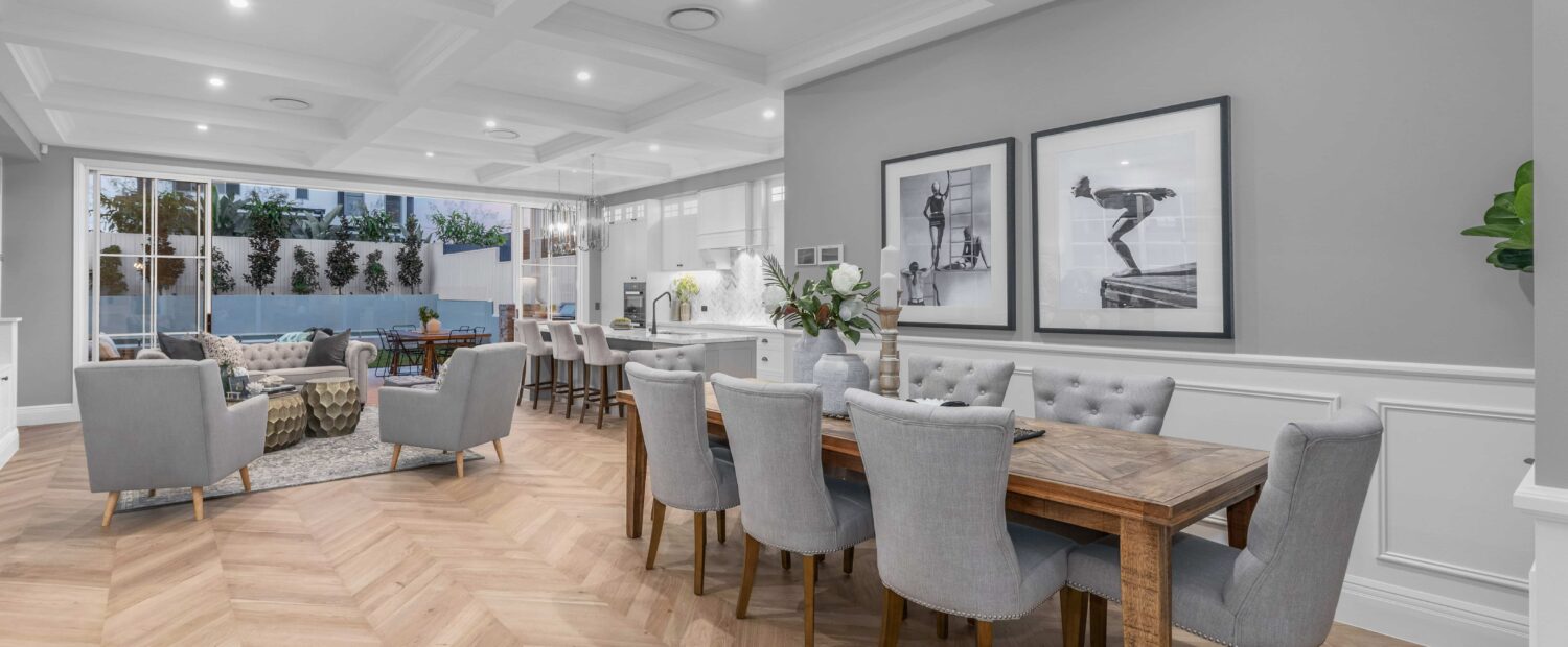 Modern Hamptons-style dining area with grey walls, white panelling, and wooden dining table with grey dining chairs