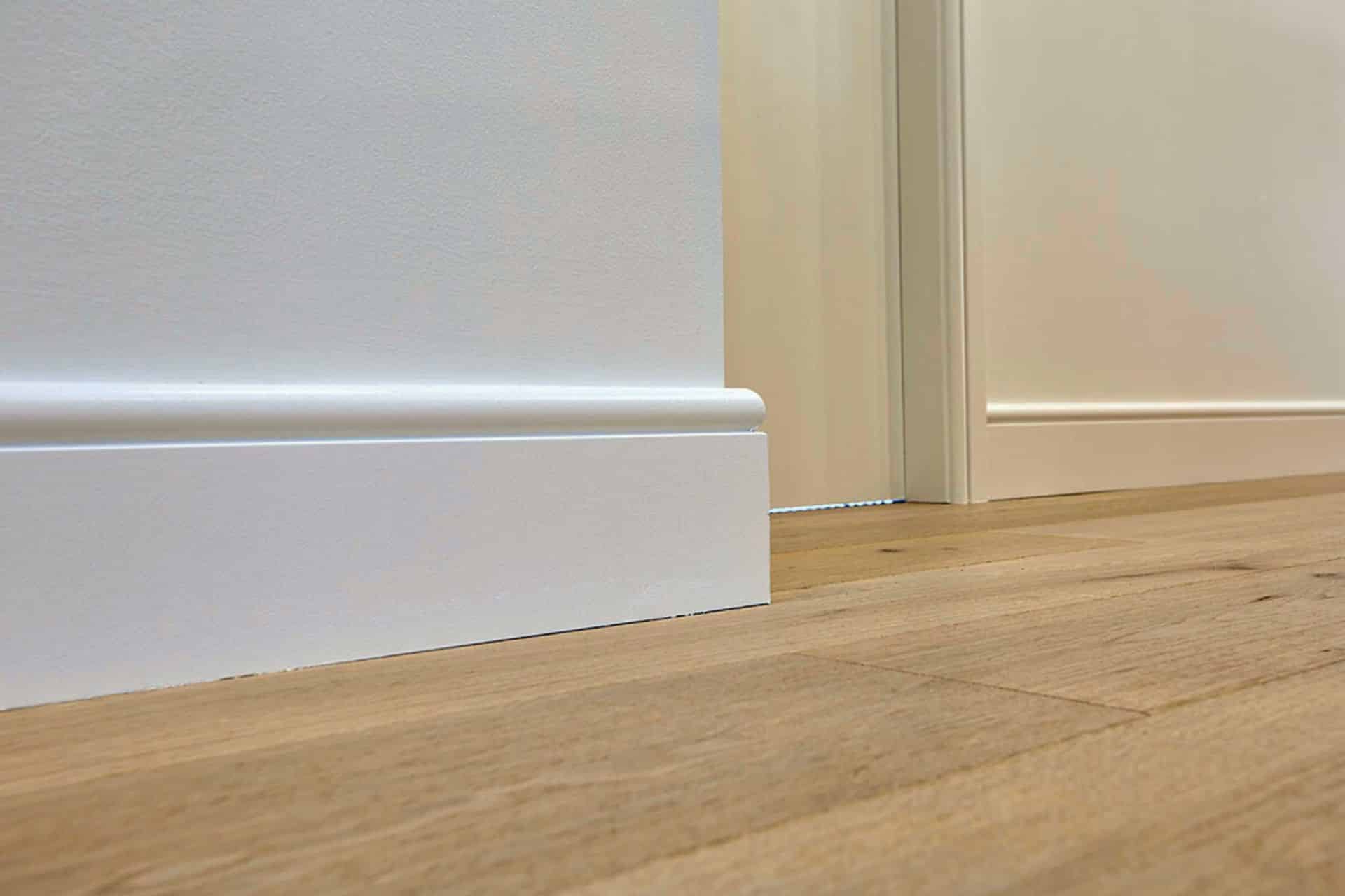 Close up of a white skirting board and wooden flooring