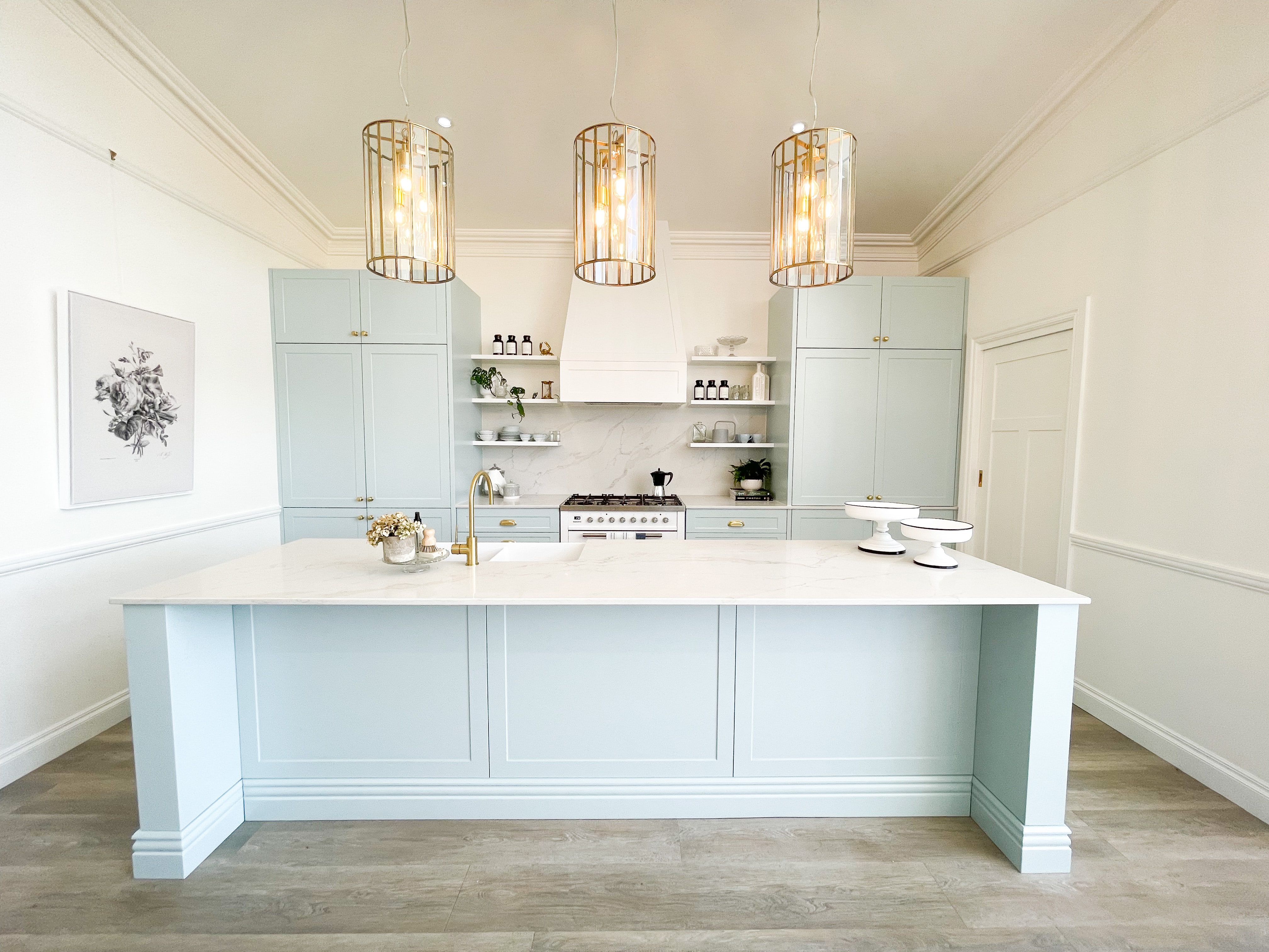 Pastel blue Hamptons kitchen with marble island, brass fittings, and a picture rail running across the wall beneath a decorative ceiling cornice.