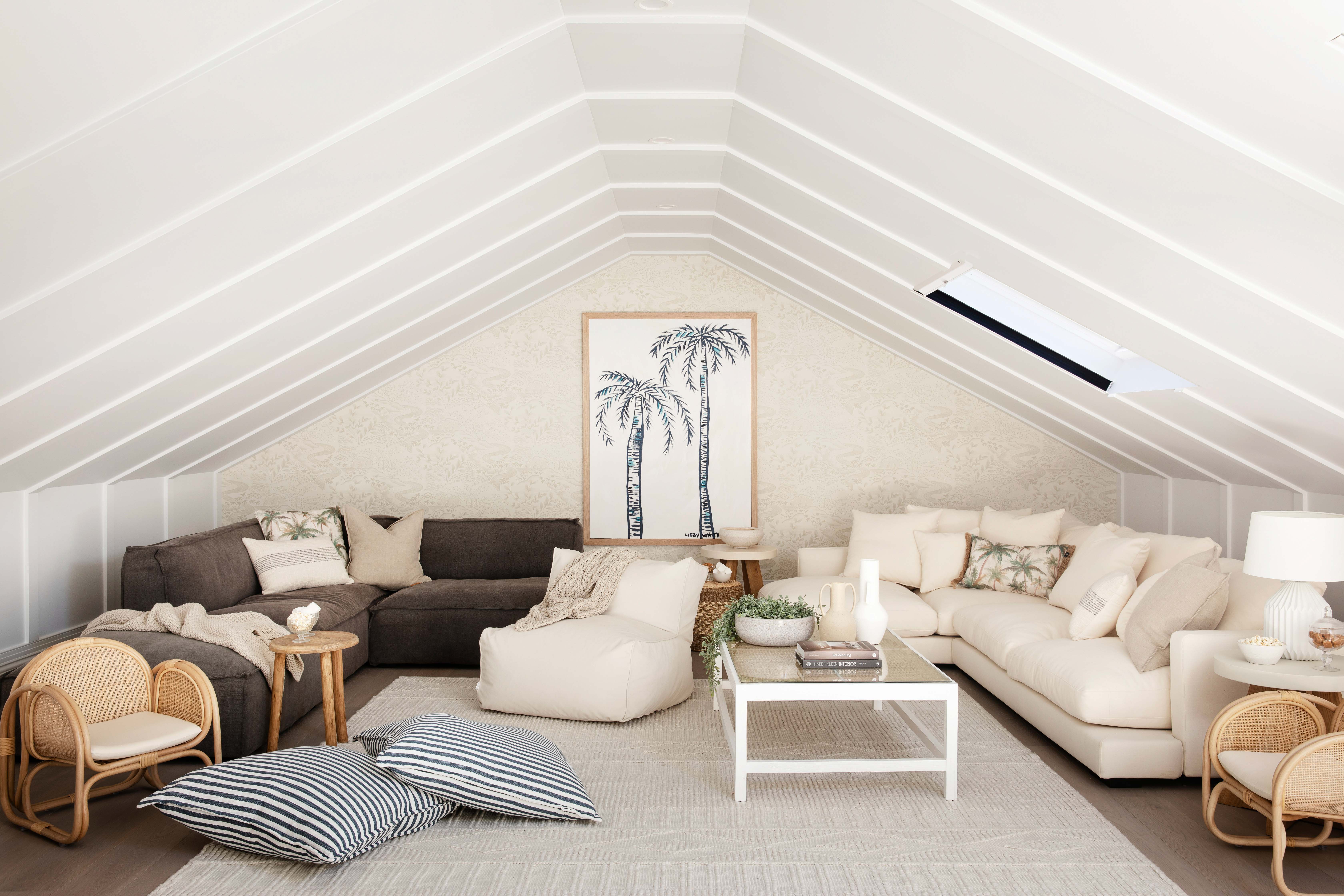 Attic living space featuring white linear ceiling panels with crisp moulded battens following the roof pitch, creating architectural rhythm above a relaxed, light-filled seating area.