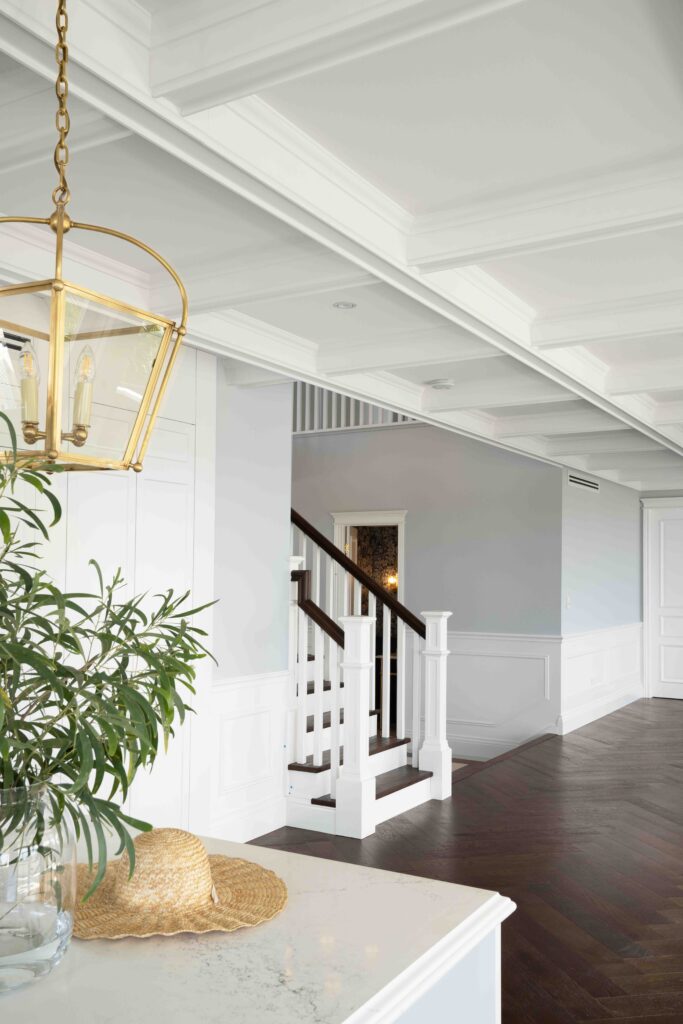 Elegant white coffered ceiling panels with layered mouldings, paired with classic wall panelling and a refined staircase