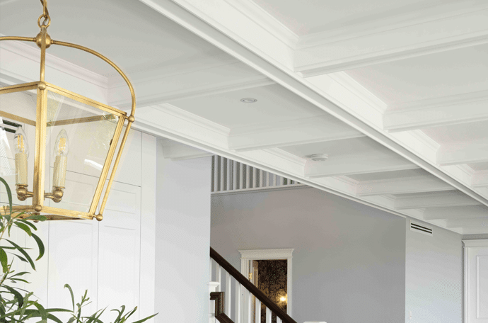 Elegant white coffered ceiling panels with layered mouldings, paired with classic wall panelling and a refined staircase