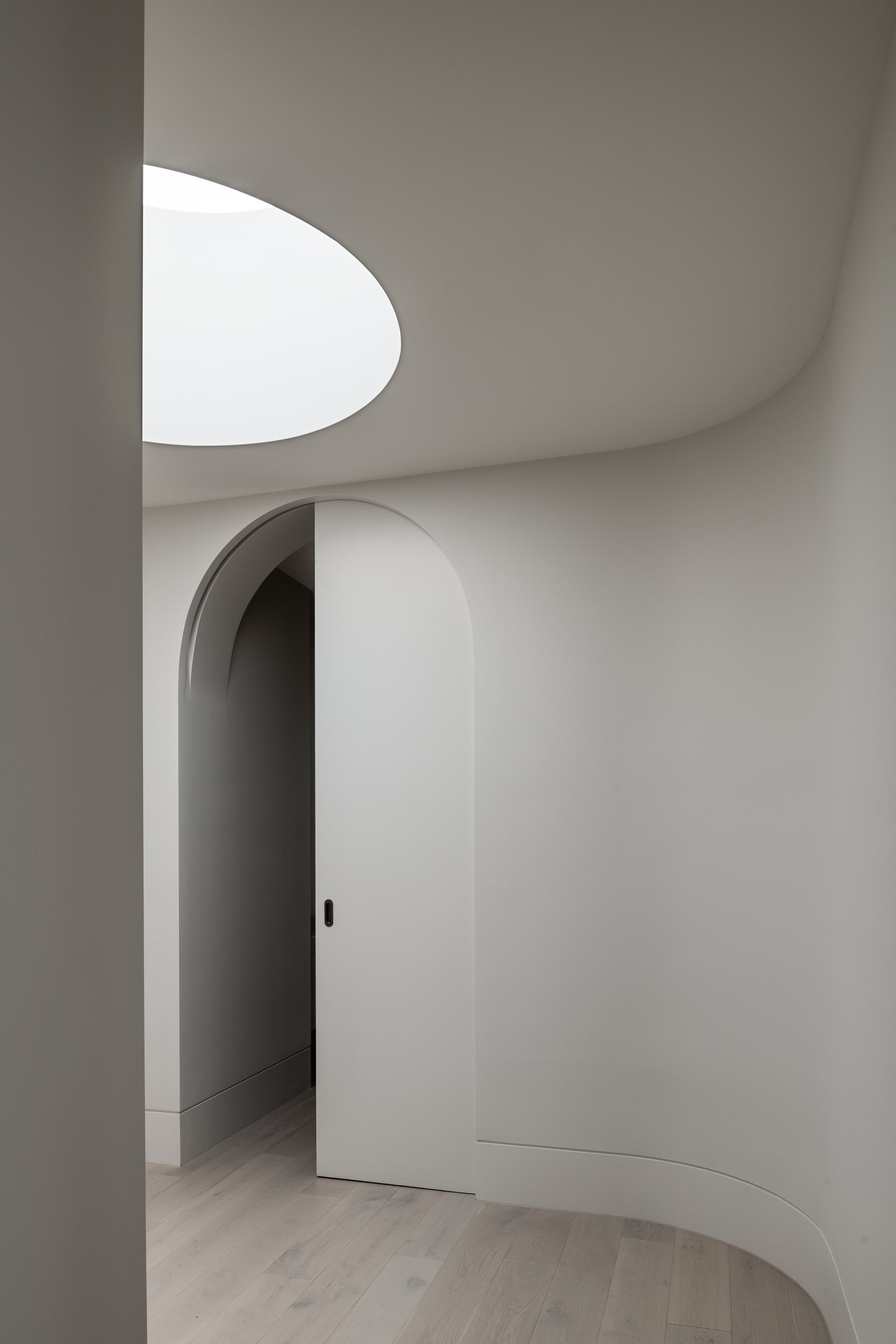 Minimalist interior with curved walls and arched doorway, showcasing subtle shadow lines and soft architectural detailing.