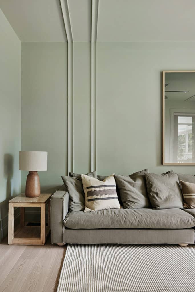 Contemporary living room with soft green wall and ceiling panelling, featuring slim vertical mouldings behind a neutral sofa.