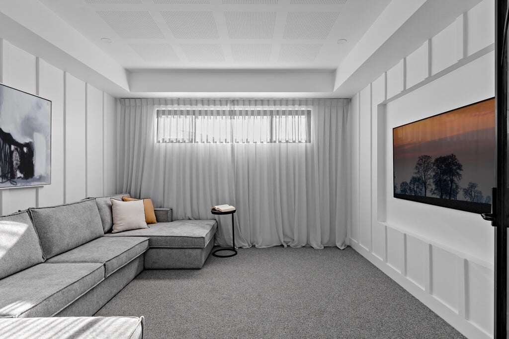 Modern Contemporary-style living space with large grey sofa, grey flooring and floor-length sheer curtain covering a horizontal window
