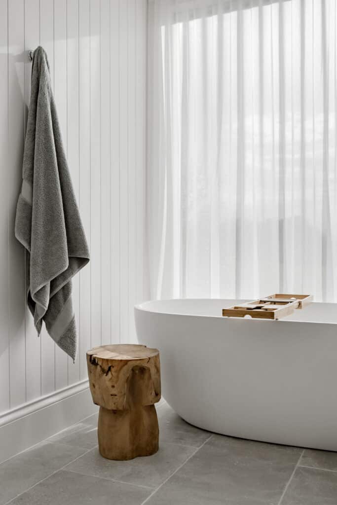 Elegant minimalist bathroom with free-standing bath, showcasing Intrim's SK445 skirting paired with Intrim's LB100 lining board on the wall. A floor to ceiling window is covered by a gauzy white curtain for a sophisticated look.