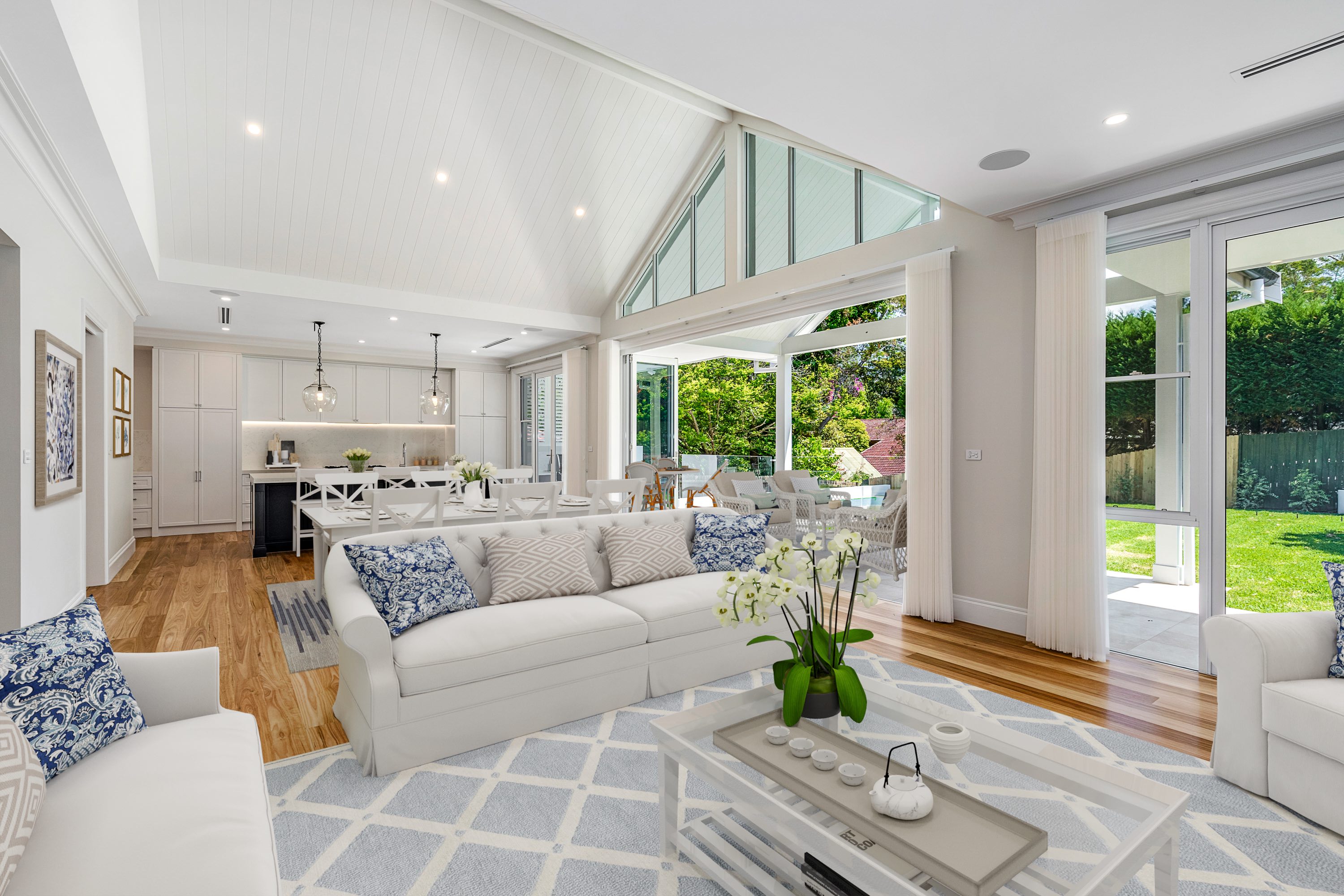 Beautifully styled Modern Hamptons open plan living room featuring light blue and white patterned rug, white 3 seater lounge and rattan style coffee table