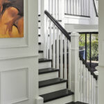 Close up of a white panelled stairway with black bannister and orange wall art