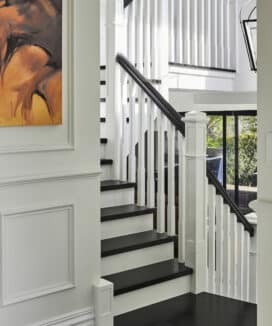 Close up of a white panelled stairway with black bannister and orange wall art