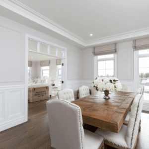 Classic Hamptons-style dining room with large wooden dining table, plush white chairs, and feature wall panelling