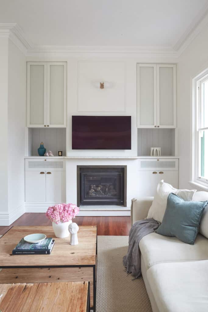 Living room with built-in cabinetry flanking a fireplace, wall-mounted TV, and soft styling—Intrim mouldings add architectural depth to a cozy, curated space.