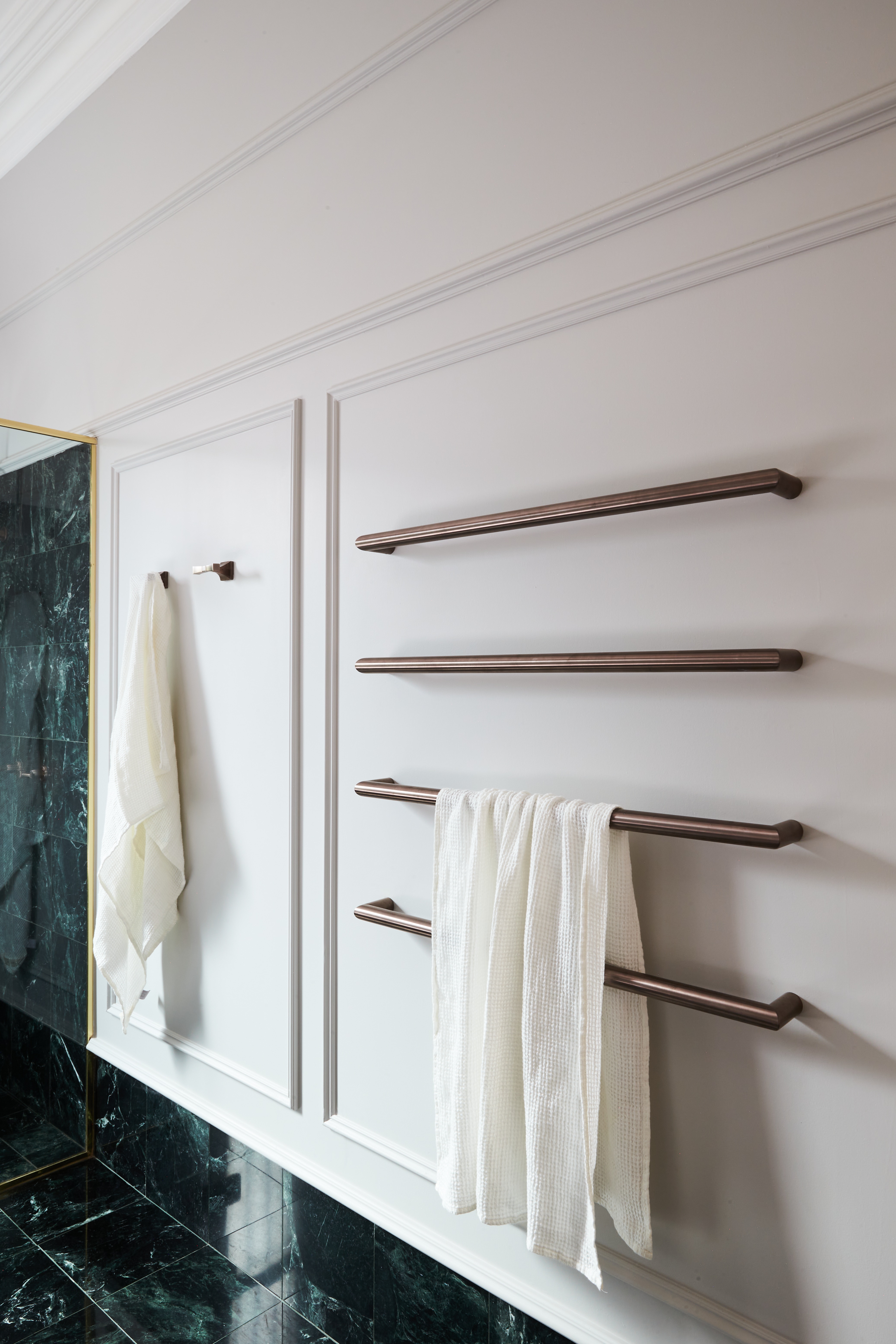 Decorative wall-mounted heated towel rails in a warm metallic finish as a contemporary contrast to classic wall panelling