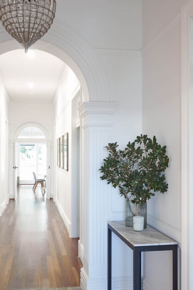 Long hallway with decorative archways and detailed mouldings—creating rhythm and visual interest in transitional zones, softened by natural light and greenery.