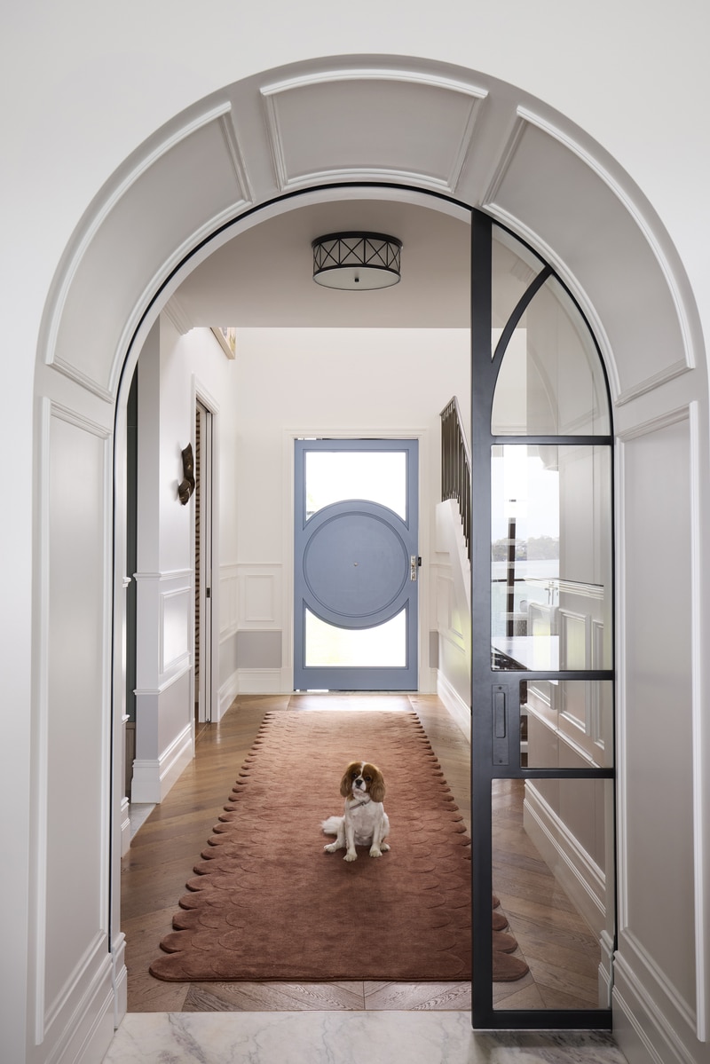 Curved MDF wall panelling following the shape of an arched doorway, with a spaniel sitting on a runner rug in the hallway beyond