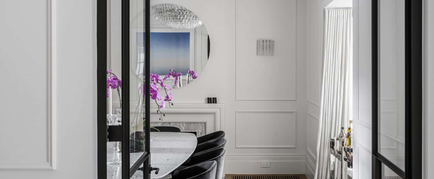 Modern dining room with white walls featuring Intrim wainscoting and skirting boards, and classic fireplace mantel under round mirror.