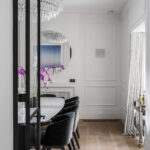 Modern dining room with white walls featuring Intrim wainscoting and skirting boards, and classic fireplace mantel under round mirror.