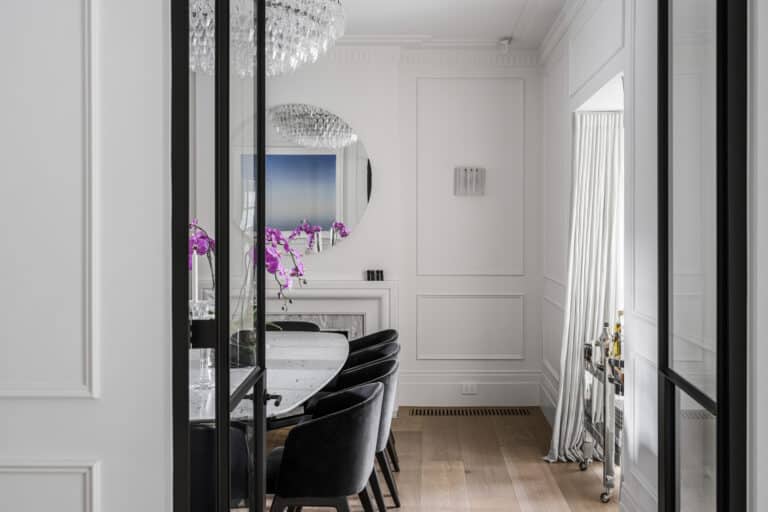 Modern dining room with white walls featuring Intrim wainscoting and skirting boards, and classic fireplace mantel under round mirror.
