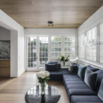 Modern sunroom with timber flooring, dark blue sectional sofa, and Intrim's premium skirting boards and VJ style wall panelling on a white wall.
