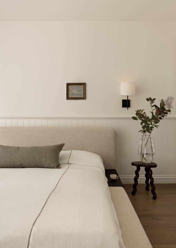 Modern bedroom with white wall panelling and dado rail, adding texture behind a neutral upholstered bed.