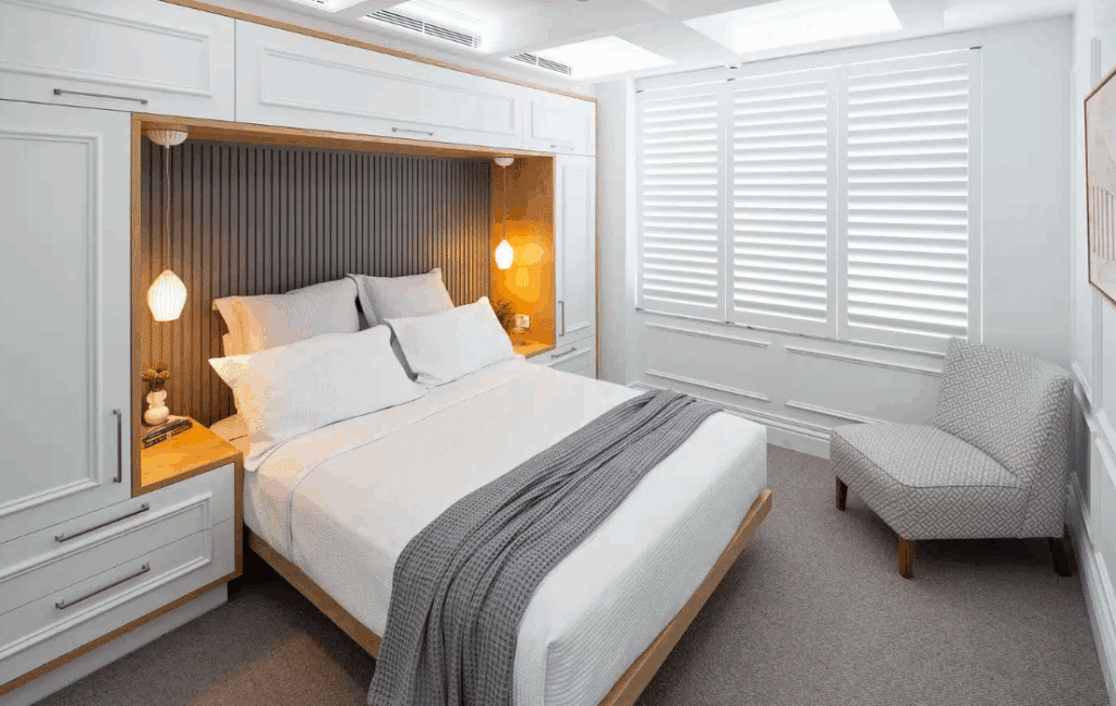 Neutral toned Modern Contemporary bedroom design featuring grey recessed wall panelling within built-in white cabinetry and accented with warm pendant lighting.