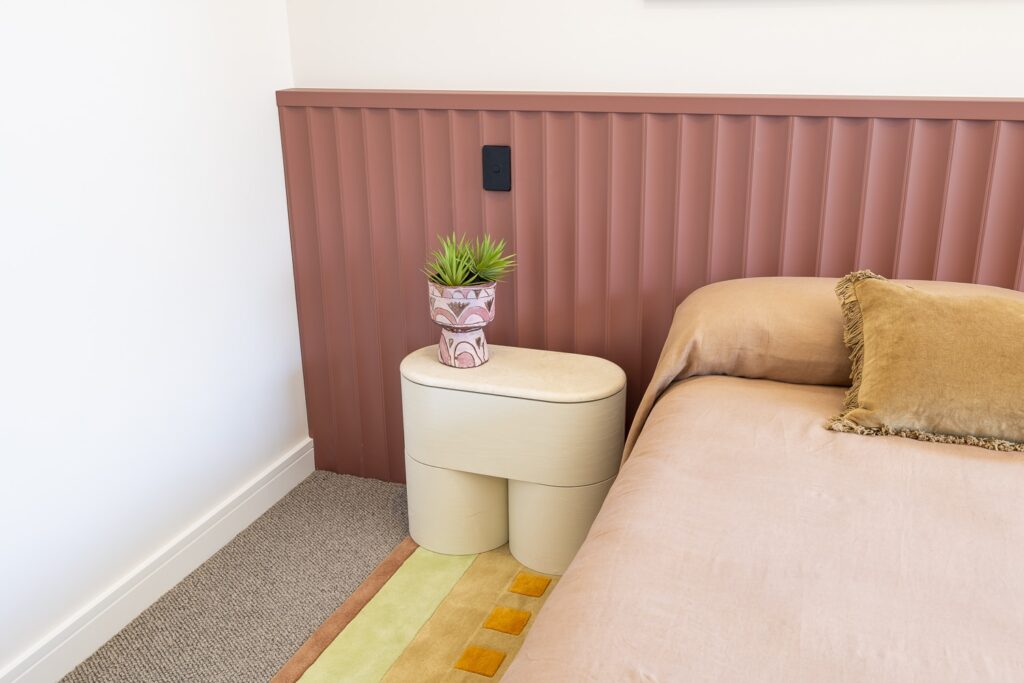 Corner of a modern contemporary bedroom design featuring dusky pink lining boards and modern furniture in shades of pink, orange, and cream.