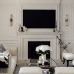 Elegant living room with decorative wall panelling framing a fireplace, layered with refined cornice detailing and a soft neutral palette.