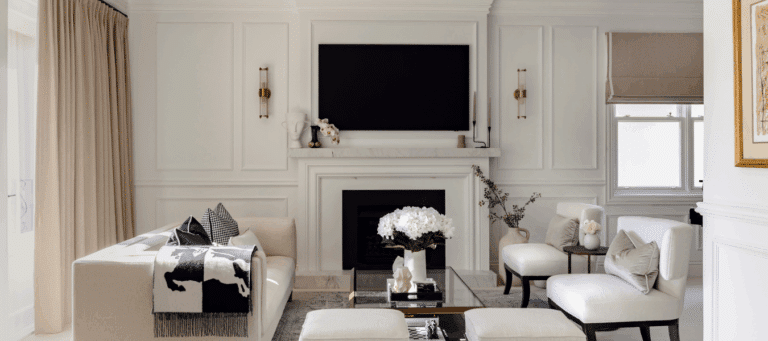 Elegant living room with decorative wall panelling framing a fireplace, layered with refined cornice detailing and a soft neutral palette.