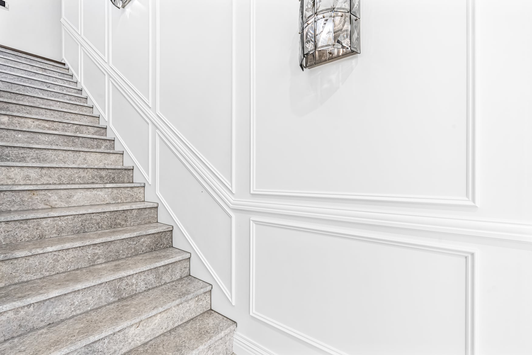 White painted stairwell wall lined with rectangular inlay mould panels stepping up alongside a stone staircase.
