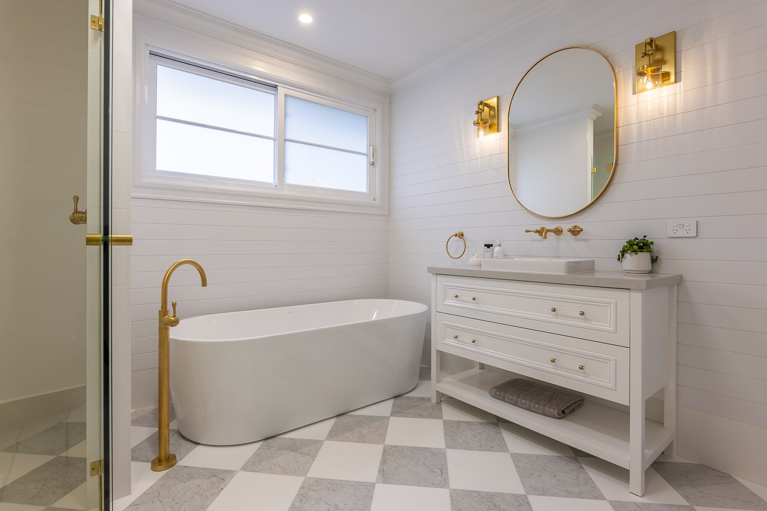 Hamptons bathroom with horizontal VJ lining board wall panelling, brass tapware, freestanding bath, and a checkerboard marble floor.