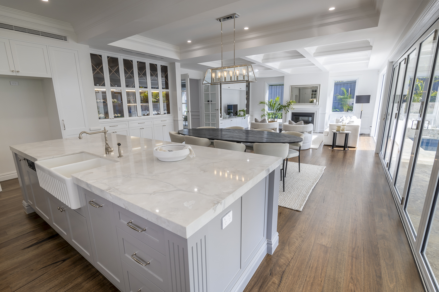 Open-plan kitchen and living area featuring decorative timber mouldings, detailed coffered ceiling panels, classic cornice, and panelled cabinetry with skirting continuity