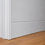 A close up of a soft, curved flush finish skirting board and coordinated curved door jamb, painted white against timber flooring.