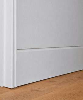 A close up of a soft, curved flush finish skirting board and coordinated curved door jamb, painted white against timber flooring.