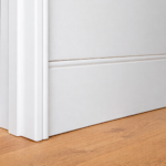 A close up of a soft, curved flush finish skirting board and coordinated curved door jamb, painted white against timber flooring.