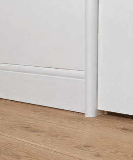 A close up shot of curved flush finish skirting board painted in white against a timber floor.