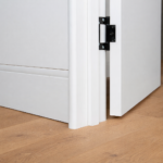 A close up of a soft, curved flush finish skirting board and coordinated curved door jamb, painted white against timber flooring.