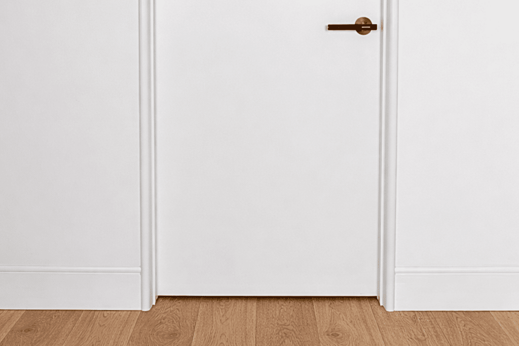 Intrim Nova Vita curved flush finish skirting and door jamb system surrounding a white door with timber flooring.