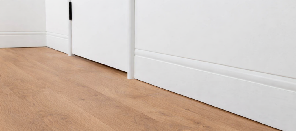 A close up shot of curved flush finish skirting board painted in white against a timber floor.