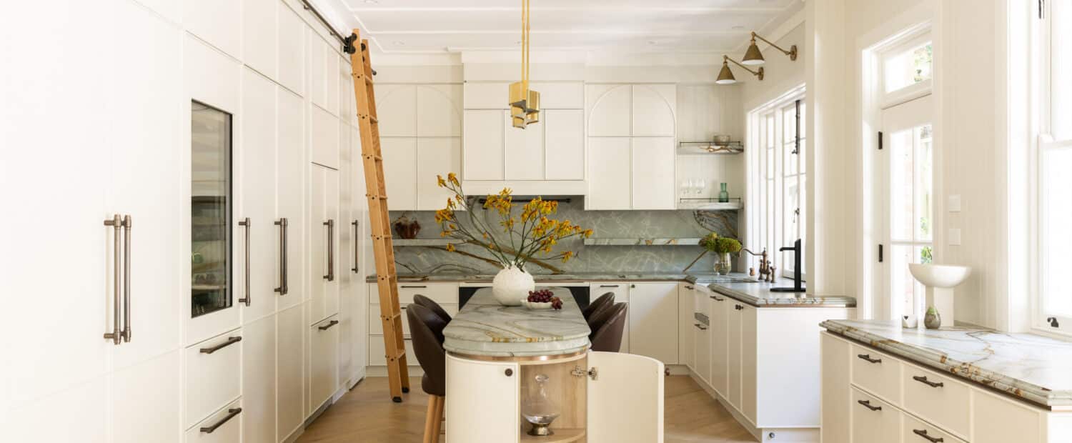 Open-plan heritage kitchen in a Neutral Bay renovation by Danielle Victoria Design Studio with floor-to-ceiling cream joinery, a timber library ladder, brass pendant and quartzite waterfall island, finished with herringbone oak floors