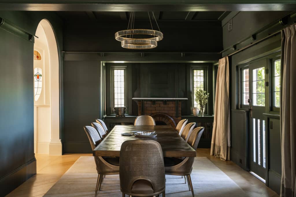 Formal dining room colour drenched in a rich green palette with a heritage brick fireplace, leadlight windows, rattan dining chairs, a tiered ring chandelier, and finished with SK498 skirting
