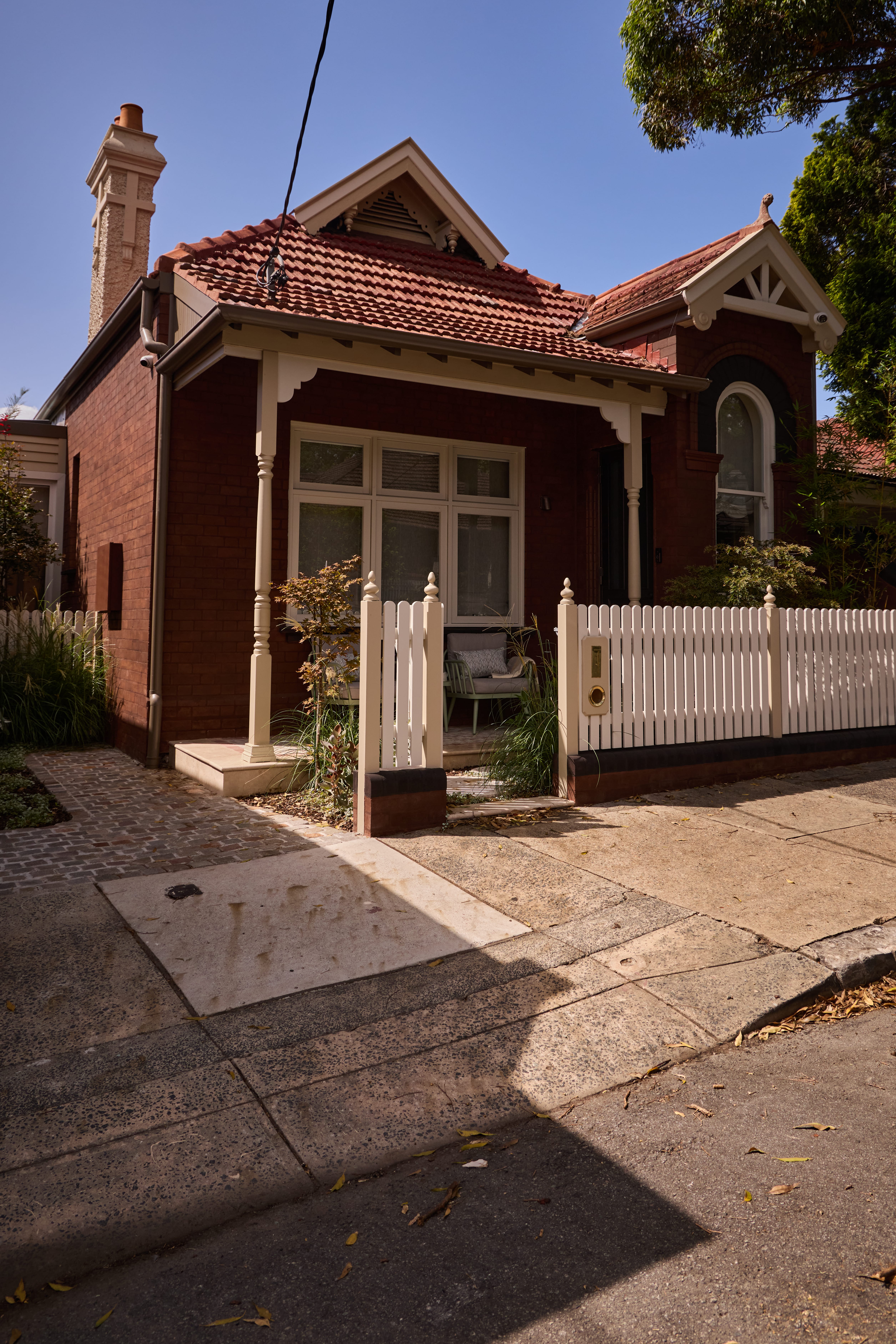California Bungalow Australia exterior with red brick façade, terracotta tile roof, gabled porch with decorative timber fretwork, and small-pane double-hung windows.
