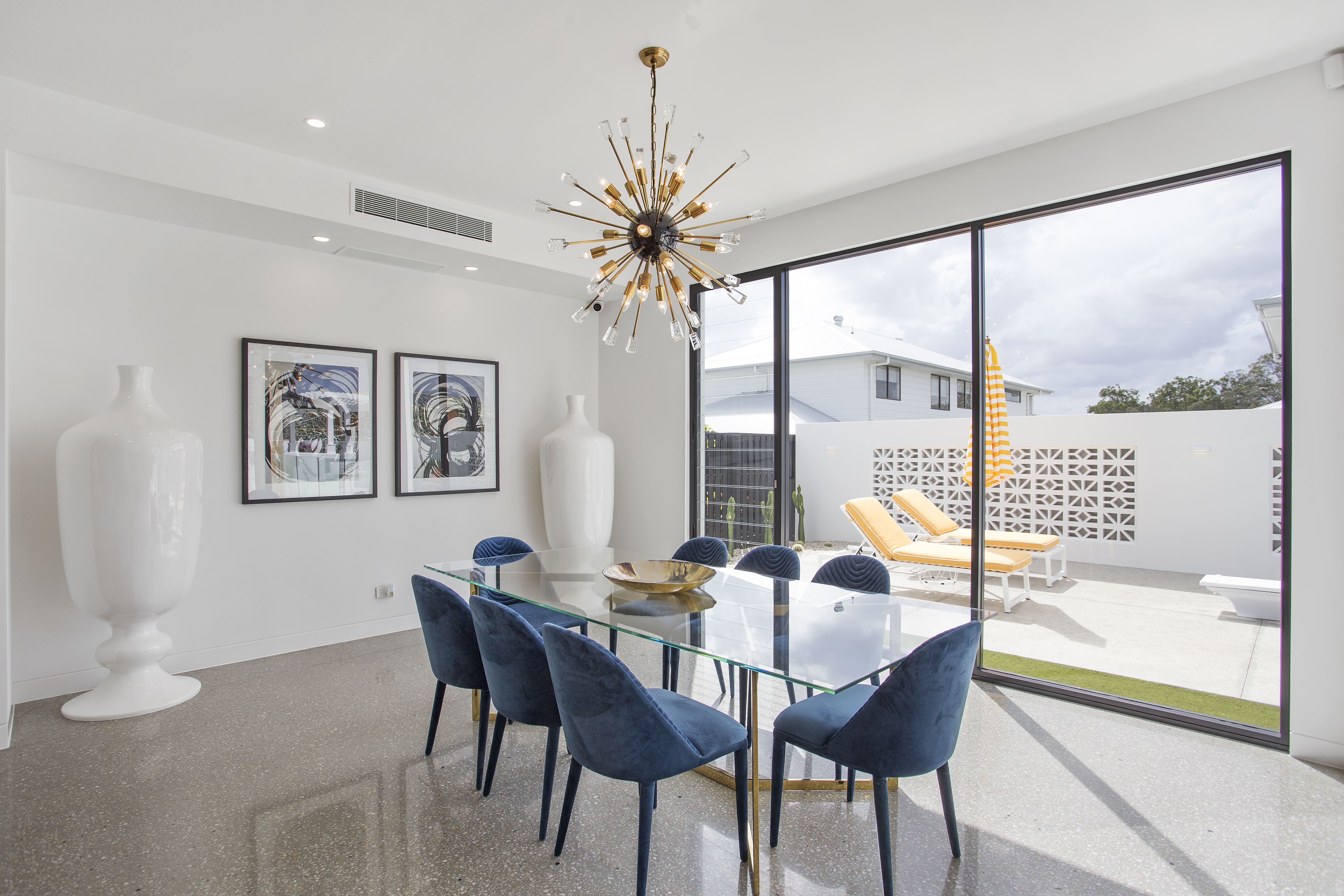 Mid-century modern Australian dining room with minimal skirting profiles, full-height sliding glass doors, sputnik chandelier, and breeze-block courtyard screen.