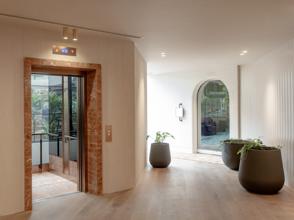 Lobby corridor at Zagame's Place Hawthorn, featuring a terracotta marble lift surround, fluted white wall panelling, large charcoal planters with greenery, and Intrim Shadowline flush skirting detailing
