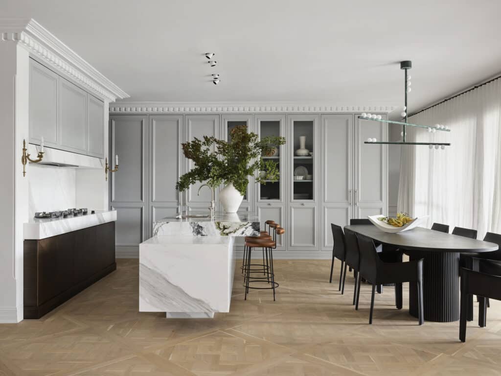 Open-plan kitchen and dining room at Matchpoint House Strathfield by Duet, featuring a marble waterfall island with dark fluted base, grey painted panelled cabinetry, brass wall sconces and herringbone oak parquetry floors